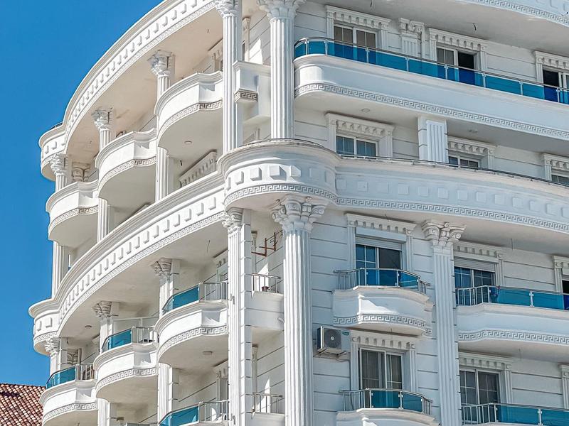Elegant white hotel with curved balconies under clear blue sky.