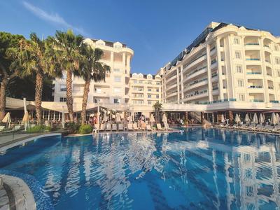 Großes Hotelgebäude mit Pools, Palmen und Sonnenschirmen unter klarem Himmel.