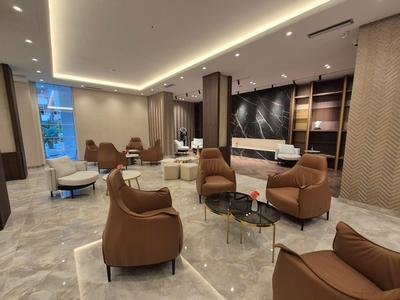 Modern hotel lobby with brown armchairs, marble floor, and warm indirect lighting.
