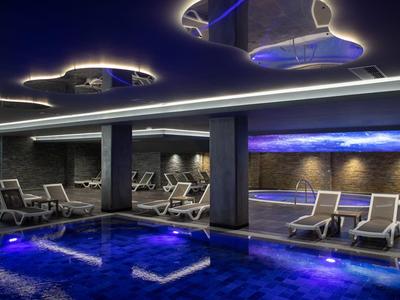 Modern indoor pool with blue lighting and lounge chairs in a luxury hotel.