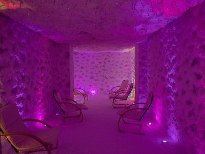 A room with rough stone walls, several chairs, and purple lighting for relaxation.