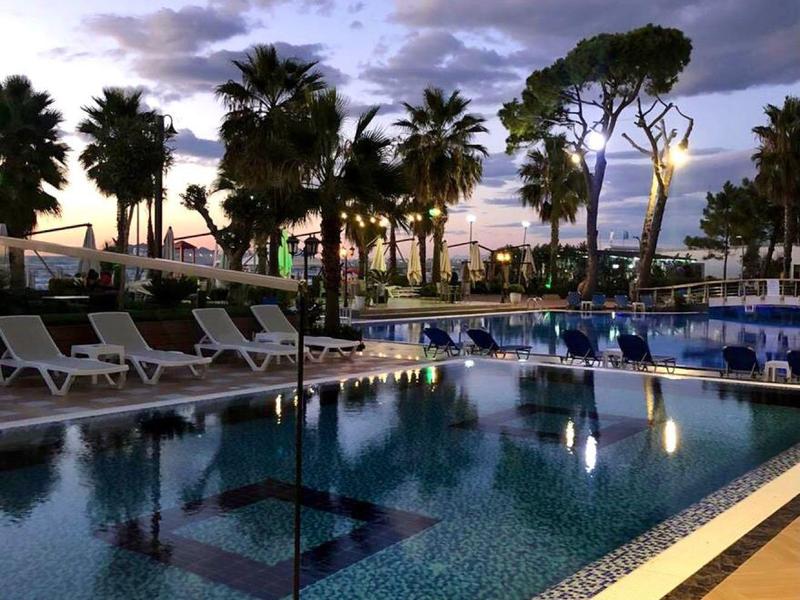 View of a lit pool with lounge chairs and palm trees at dusk.