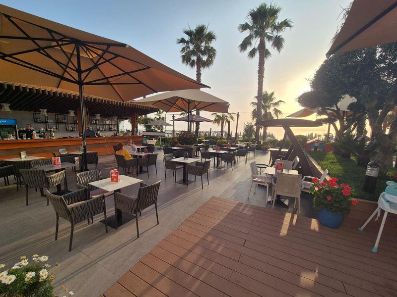 Outdoor restaurant area with tables, chairs, and umbrellas, palm trees in the background at sunset.