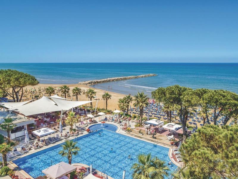 View of hotel pool with palm trees and sea in the background under clear sky