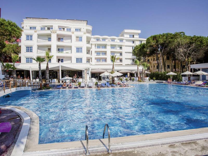 Large outdoor pool in front of multi-story hotel building with umbrellas and lounge chairs.