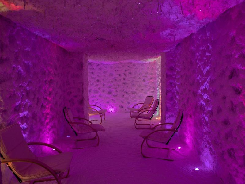 A room with rough stone walls, several chairs, and purple lighting for relaxation.