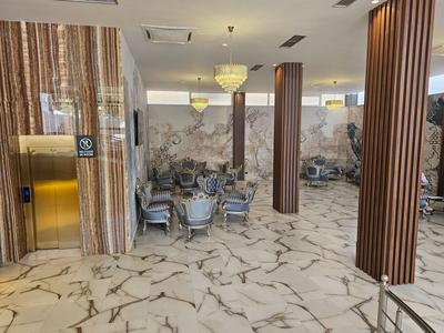 Großer Hotel-Loungebereich mit Marmorfußboden, goldfarbenem Aufzug und Tischen mit Stühlen.