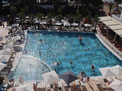 Belebter Hotelpool mit Sonnenschirmen und Gästen, umgeben von Liegestühlen und einer Bar.