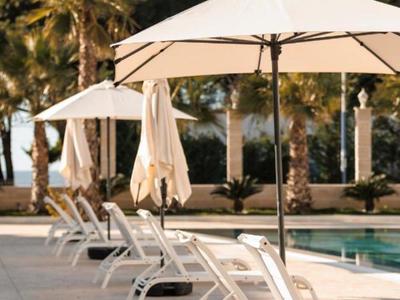 Weiße Liegestühle und Sonnenschirme neben einem Pool mit Palmen im Hintergrund.