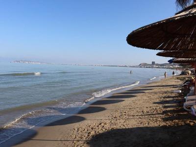 Strand mit Sonnenschirmen aus Stroh und ruhigem Meer unter klarem blauem Himmel.