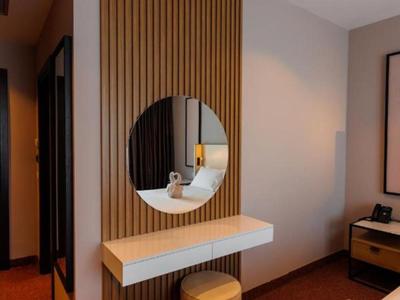 Moderner Hotelbereich mit Holzpaneel, rundem Spiegel und beigem Sitzhocker.