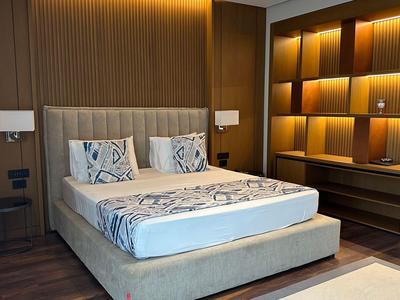 Camera d'hotel moderna con letto matrimoniale, illuminazione calda e scaffali in legno decorativi con luci.