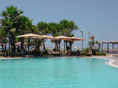 Großer Außenpool mit Sonnenschirmen, Palmen und Sitzgelegenheiten unter klarem Himmel.