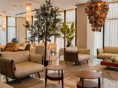 Moderner Hotel-Loungebereich mit bequemen Sesseln, hölzernen Tischen und dekorativem Baum.