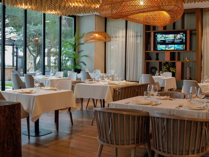 Elegantes Restaurant mit Holzboden, großen Fenstern und gehobener Tischdekoration.