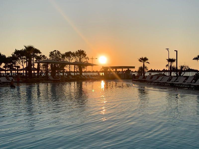 Sonnenuntergang über einem ruhigen Pool mit Palmen und Liegen am Beckenrand.