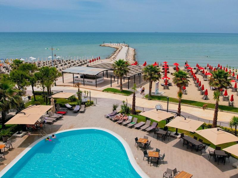 Blick auf einen Hotelpool mit Liegen und Sonnenschirmen am Strand mit Meerblick.
