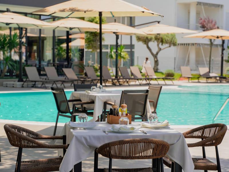 Tisch mit weißen Tüchern und Stühlen neben dem Pool vor Sonnenschirmen in einem Hotelgarten.