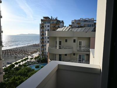 Výhled z balkonu na sousední budovy, bazén a pláž u moře.