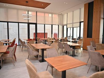 Světlý moderní hotelový salonek s dřevěnými stoly a pohodlnými židlemi u velkých oken.