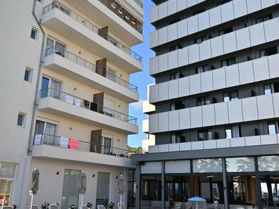 Moderní hotelový bazén mezi dvěma vícepodlažními budovami pod jasnou oblohou.