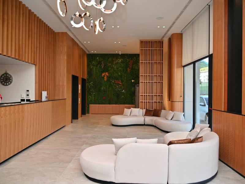 Moderní hotelová lobby s dřevěnými panely, kulatými pohovkami a zelenou stěnou rostlin.