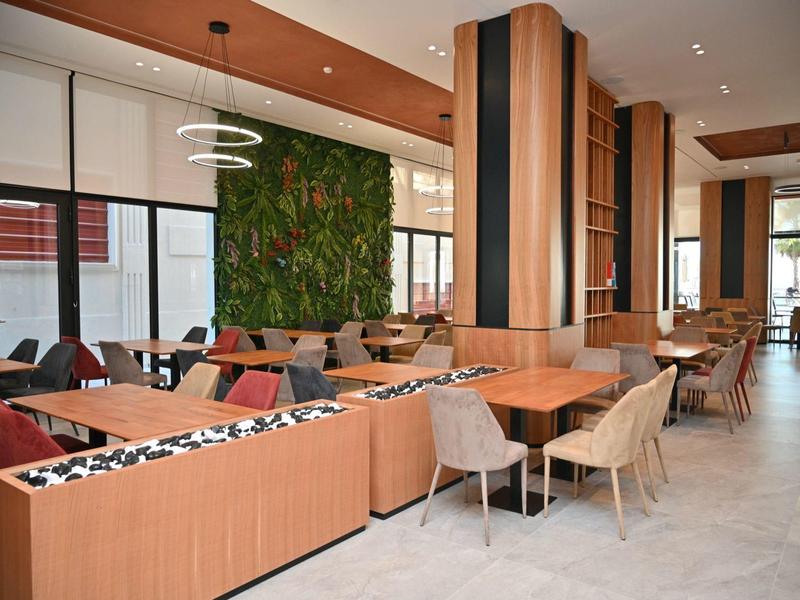 Moderní restaurace se dřevěnými panely, pohodlnými židlemi a zelenou nástěnnou výzdobou.