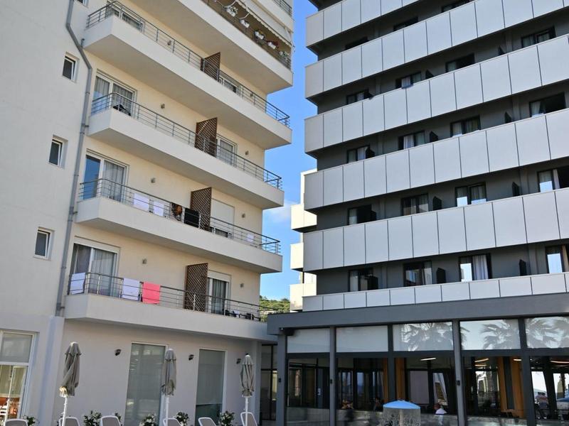 Moderní hotelový bazén mezi dvěma vícepodlažními budovami pod jasnou oblohou.