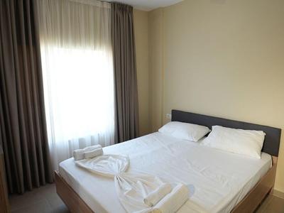 Schlichtes Hotelzimmer mit Doppelbett, weißen Bettwäsche, Handtüchern und Vorhängen am Fenster.