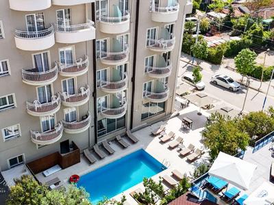Blick auf ein Hotel mit Außenpool und Sonnenliegen, umgeben von Straßen und Grünflächen.