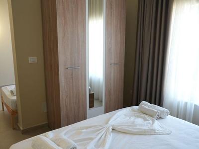 Hell eingerichtetes Hotelzimmer mit Doppelbett, Schrank mit Spiegel und Vorhängen am Fenster.