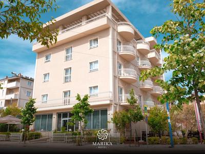 Ein mehrstöckiges helles Hotelgebäude mit Balkonen und umgeben von Bäumen unter blauem Himmel.