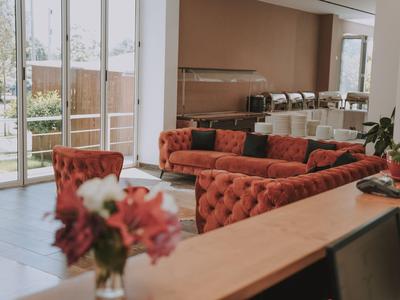 Gemütlicher Hotel-Loungebereich mit rot gepolsterten Sofas, Holztisch und großem Fenster.