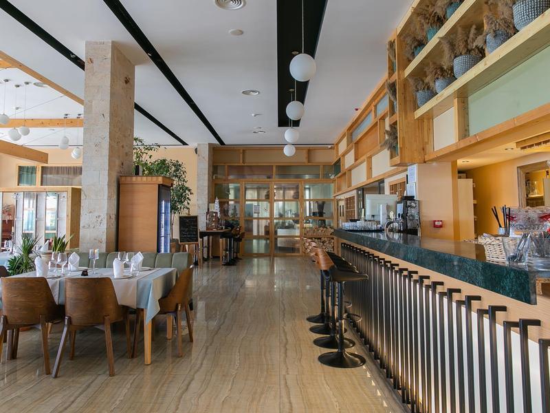 Modern restaurant area with wooden furniture, set tables, and a bar with stools.