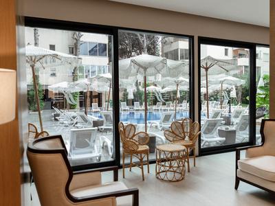 Blick durch große Fenster auf eine Terrasse mit weißen Sonnenschirmen und Stühlen neben einem Pool.