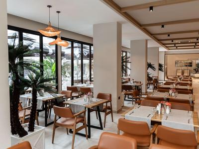 Stylisches Hotelrestaurant mit Holztischen, bequemen Stühlen und großen Fenstern mit Blick auf Pflanzen.