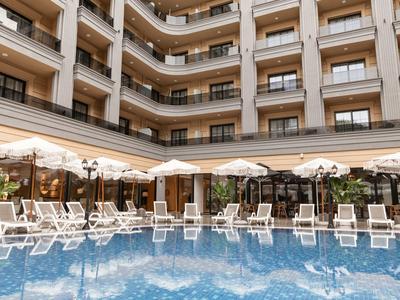 Hotelpool mit Liegestühlen und Sonnenschirmen vor einem mehrstöckigen Hotelgebäude