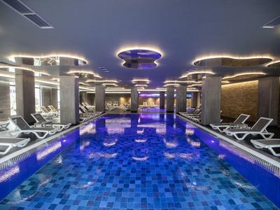 Modernes beheiztes Hallenbad mit blauem Mosaikfliesenboden und weißen Liegen