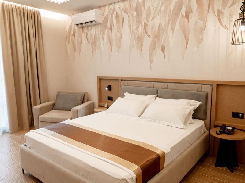 Gemütliches Hotelzimmer mit Doppelbett, Sessel, Nachttischen und einer dekorativen Wandgestaltung.