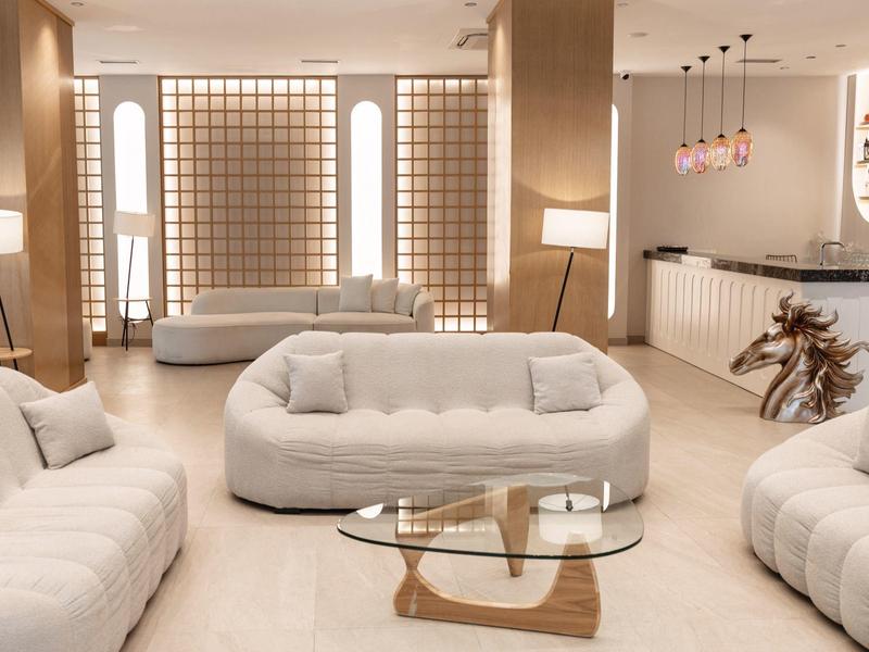 Helles Wohnzimmer mit drei weißen Sofas, einem Glastisch und moderner Beleuchtung.