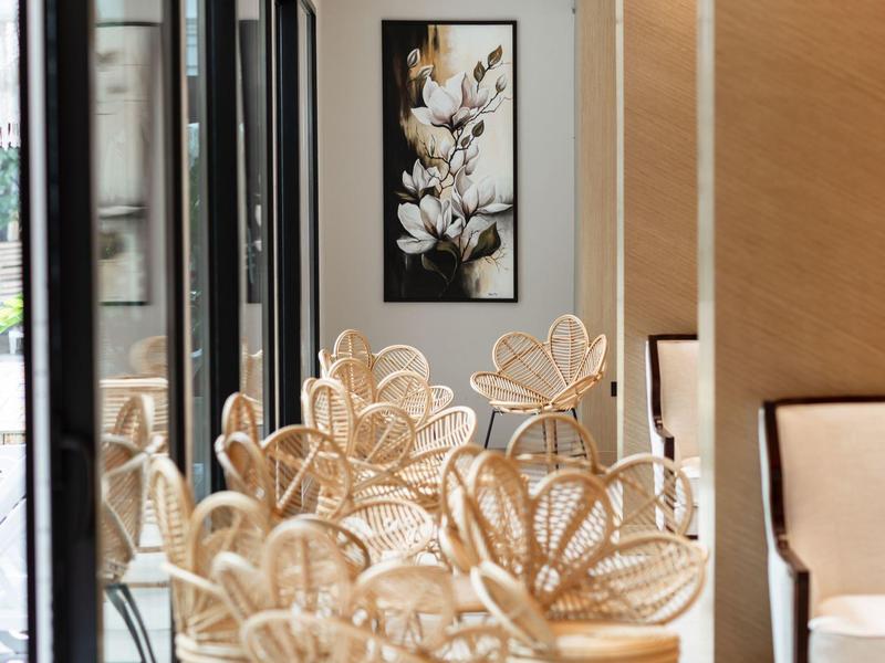 Heller Gastraum mit geflochtenen Stühlen und Blumenbild an der Wand.