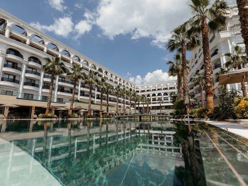 Großes Hotel mit Poolfront, umgeben von Palmen und blauem Himmel mit Wolken.
