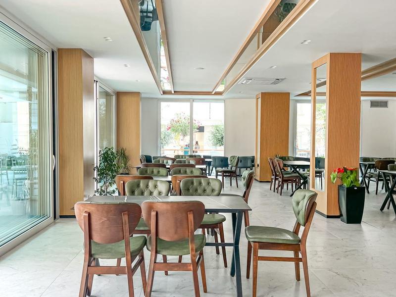 Helles, modernes Restaurant mit großen Fenstern, Holzmöbeln und grünen Pflanzen.