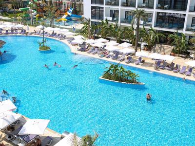 Großer Außenpool mit Liegestühlen und Menschen, umgeben von Hotelgebäuden und Palmen.