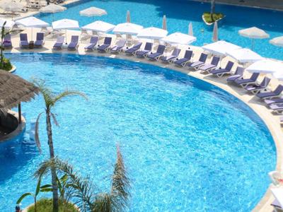 Großer Hotelpool mit vielen Liegestühlen und Sonnenschirmen in U-Form.