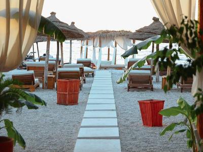 Freundlicher Strand mit Liegestühlen, Sonnenschirmen und einem Steg, der zum Wasser führt.