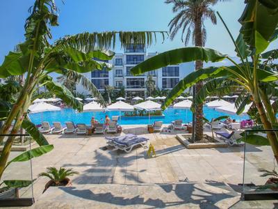 Hotelpool mit Sonnenschirmen und Liegestühlen, umgeben von Palmen und einer großen Hotelanlage im Hintergrund