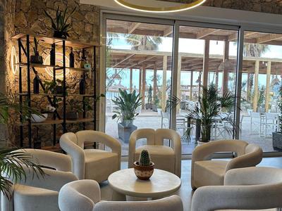 Salon d'hôtel confortable avec fauteuils, plantes et grande fenêtre donnant sur la terrasse.