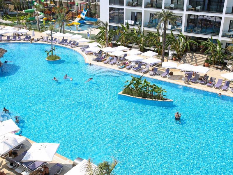 Großer Hotelpool mit Sonnenschirmen, Liegestühlen und Menschen im Wasser.