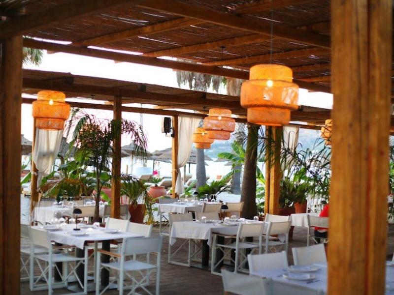 Überdachter Außenbereich eines Restaurants mit weißen Tischen und Stühlen sowie orangefarbenen Lampen.